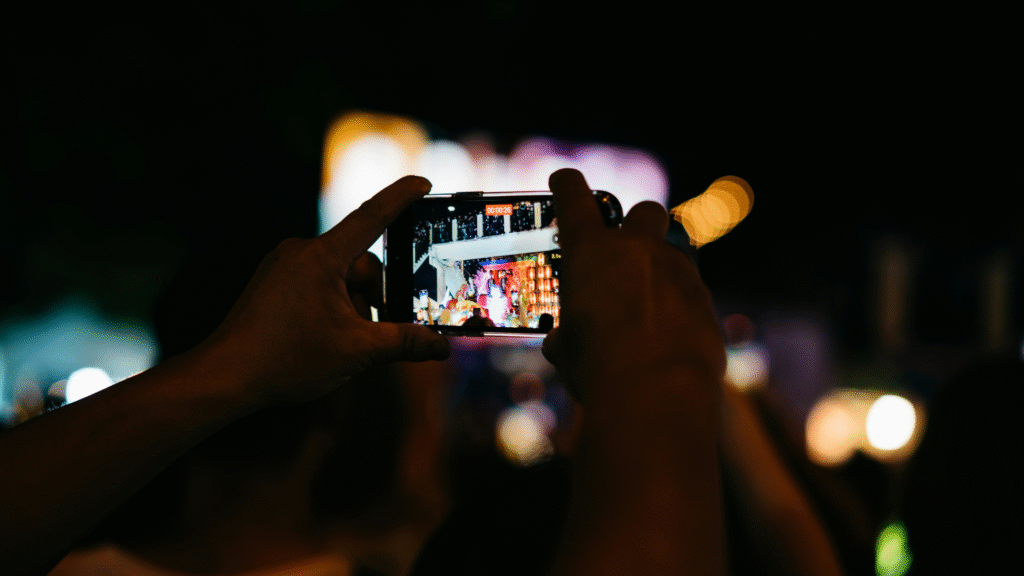 Hands holding a mobile filming a colourful stage at nighttime.