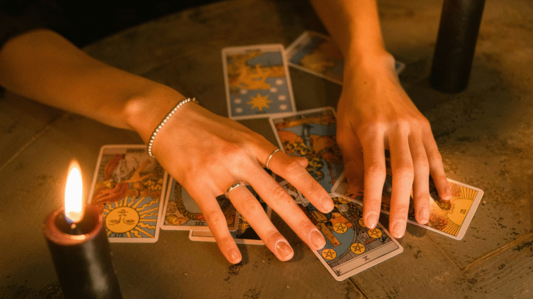 Candlelit hands of a white woman hovering over tarot cards